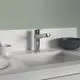 Küchenarmatur von Ideal Standard mit einem hohen Auslauf. Sie ist in Chrom gehalten und montiert auf einer weißen Arbeitsfläche, neben Geschirr und einem schwarzen Schalen.